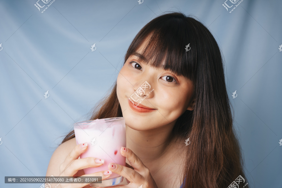 亚洲年轻女子手持一杯粉红色奶昔的特写照片。