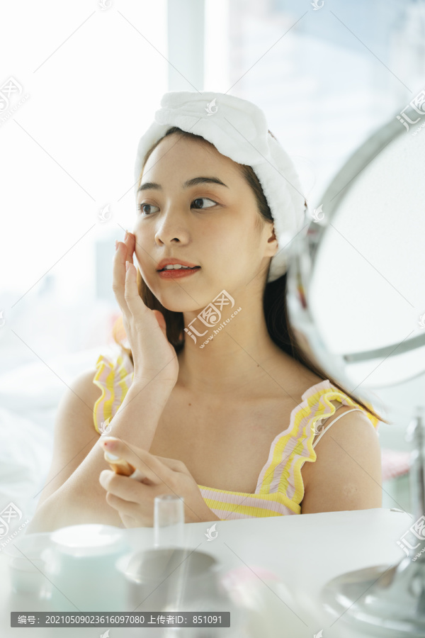 年轻的亚洲黑发女性在镜子前使用面部美容护肤品。