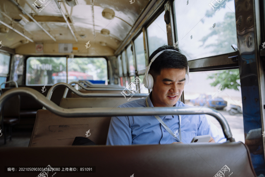 在曼谷的一辆公共汽车上，亚洲商人用无线耳机听音乐。