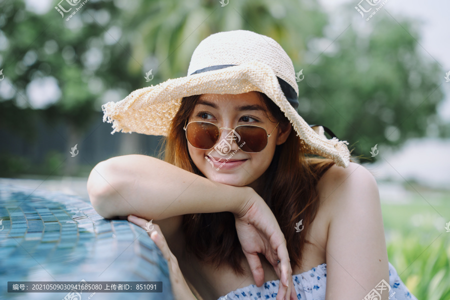 特写肖像-美丽的亚洲女游客，戴着太阳镜和帽子在泳池边。
