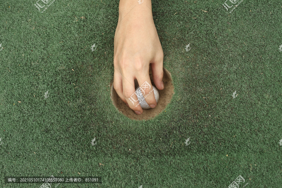 把高尔夫球从洞里拿出来的人放在果岭上，特写，俯视，专注于手和高尔夫球。