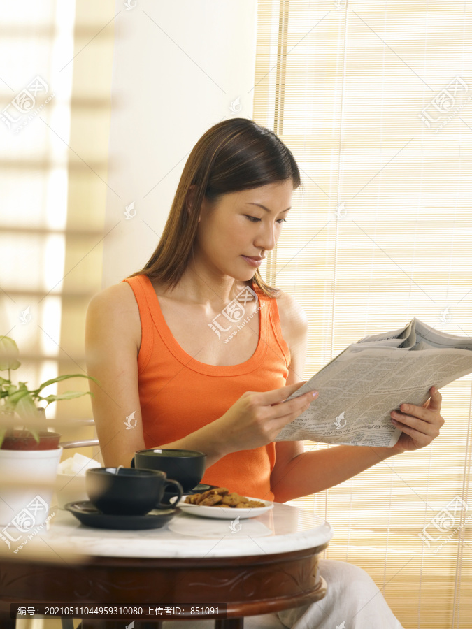年轻女子一边看报纸一边喝茶