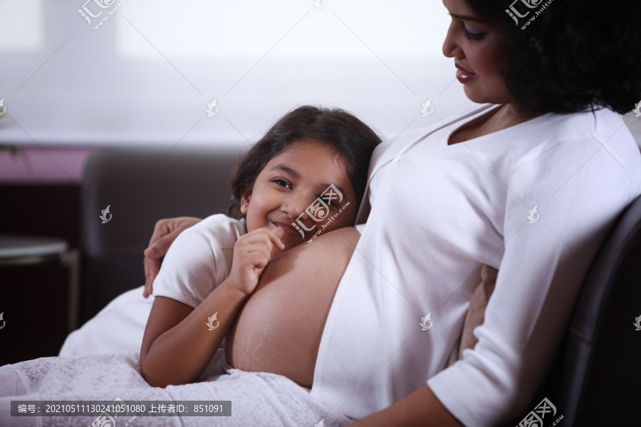 小女孩耳朵贴着妈妈怀孕的肚子
