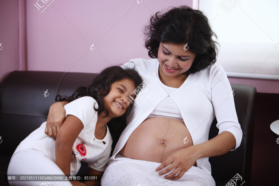可爱的母女照片与女儿笑着妈妈怀孕的肚子。