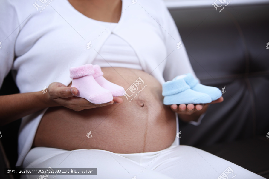 孕妇抱着粉红和蓝色婴儿靴
