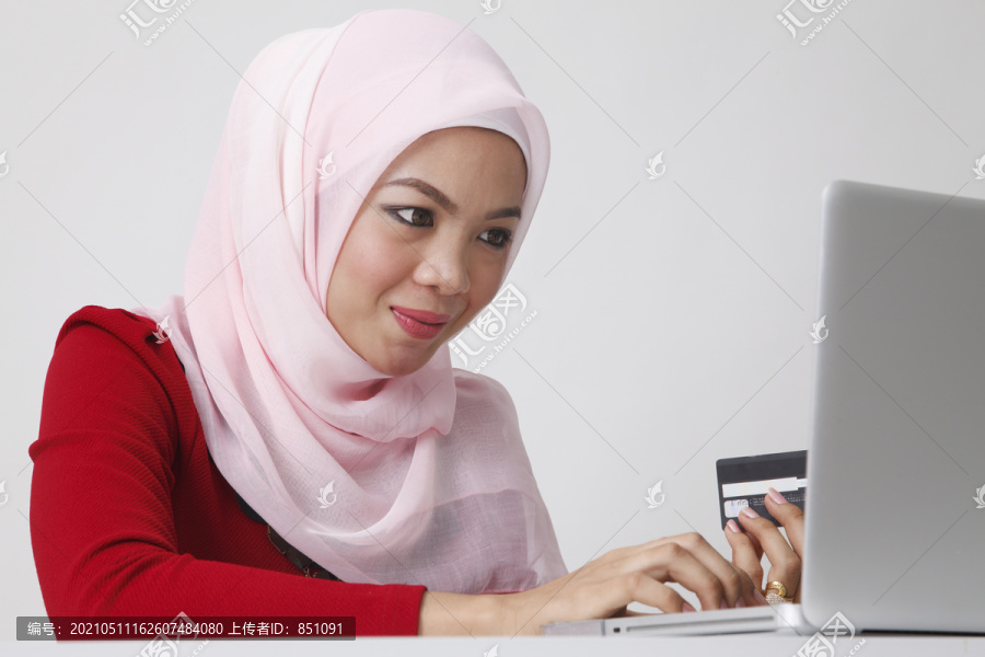 头巾坐在手提电脑前拿着信用卡