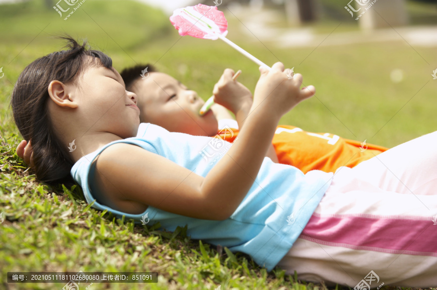 男孩和女孩躺在草地上，吃着棒棒糖
