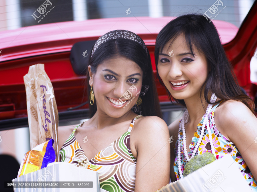 女人们在超市停车场提着购物袋，微笑着
