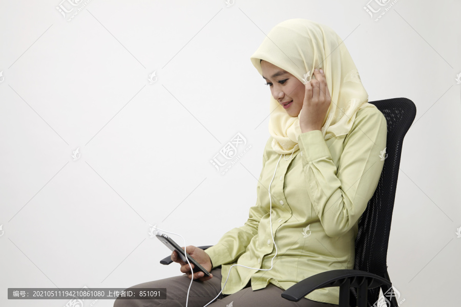 马来妇女坐在办公椅上听音乐