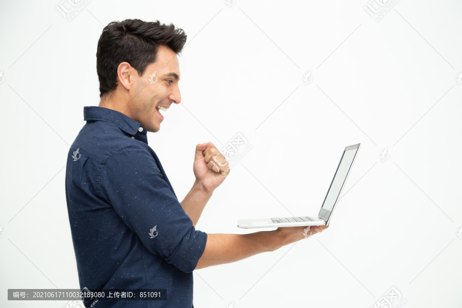 一名兴奋的男子手持笔记本电脑，在白色背景下庆祝成功，带着幸福的表情举起手臂，男性模特