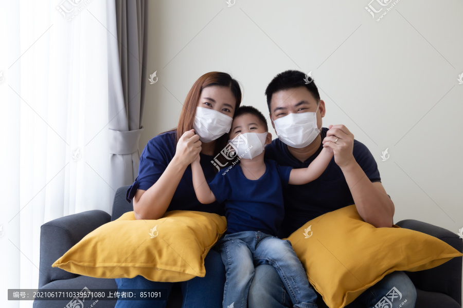 亚洲家庭戴2019冠状病毒疾病预防罩，并在客厅里一起坐在一起。保护家庭免受空气污染概念