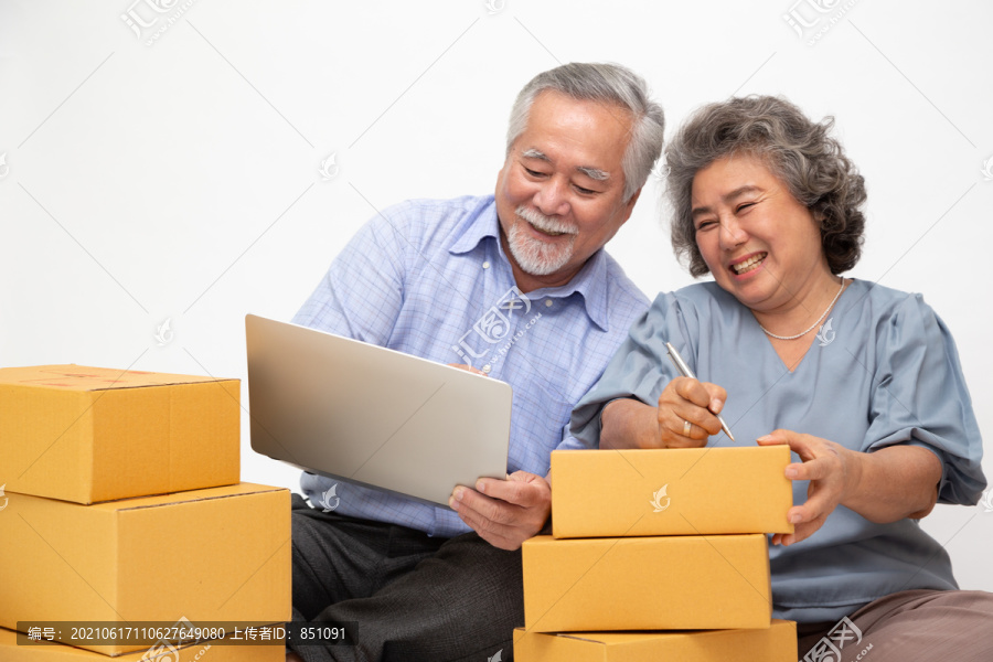 亚洲资深夫妇创业小型企业自由职业者，带着包裹盒和笔记本电脑，坐在白色背景的地板上，在线营销包装盒交付