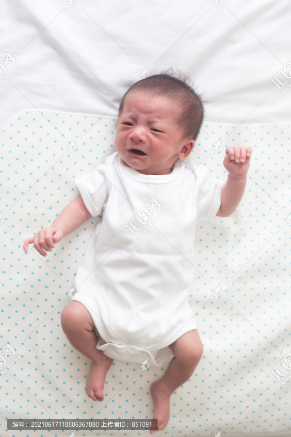 俯视图：亚洲男婴躺在白色的床上，哭着肚子痛