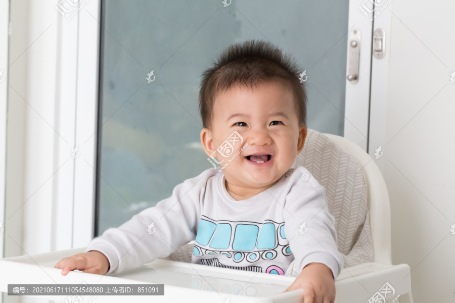 快乐的亚洲男婴在餐桌旁等待食物