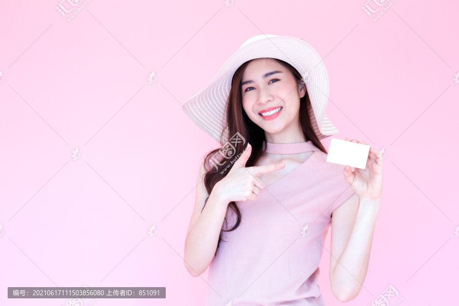 美丽的年轻亚洲女性微笑着出示带有复印空间粉色背景的信用卡，在线购物或机票付款，电子商务概念