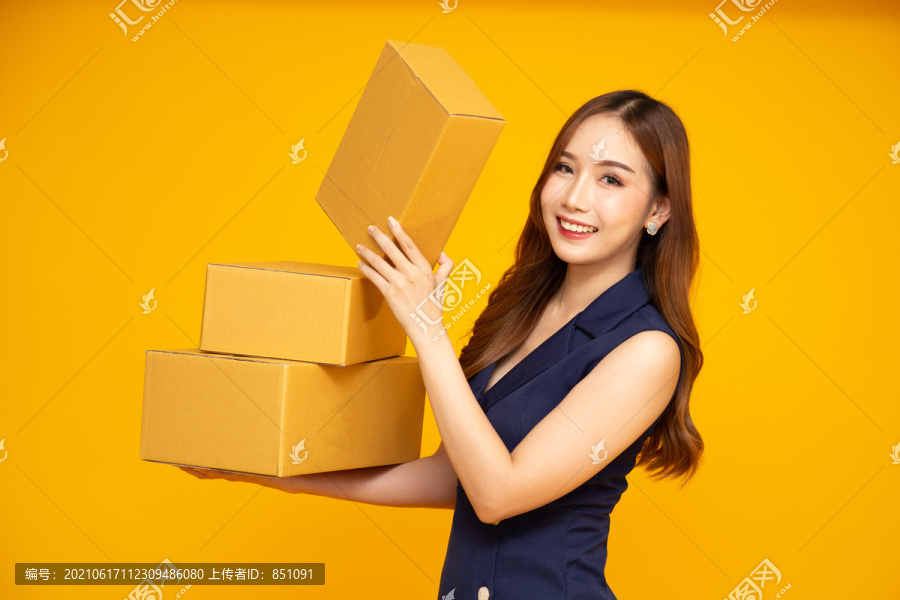 快乐的亚洲女人微笑着拿着黄色背景上隔离的包裹盒，快递和运输服务理念