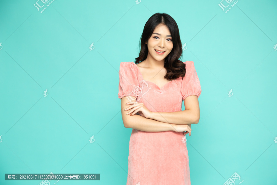 成功的商业亚洲女性肖像，身穿粉红色连衣裙，双臂交叉，微笑孤立于绿色背景之上