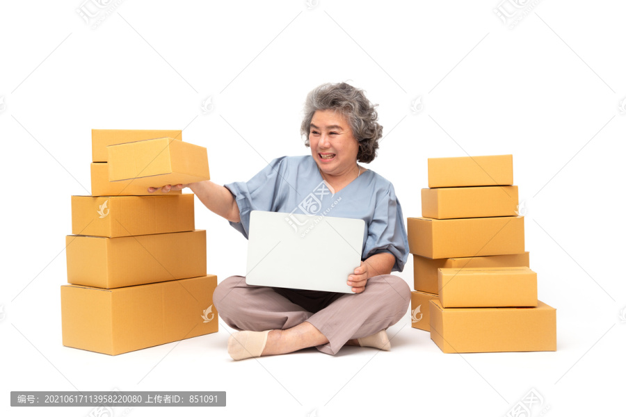 亚洲资深女性创业小企业自由职业者，手拿包裹盒和笔记本电脑，坐在白色背景的地板上，在线营销包装盒交付概