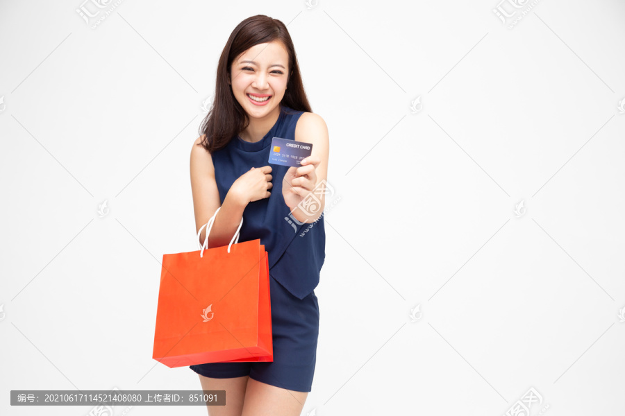 一个快乐的年轻女子手持购物袋和信用卡的肖像，在白色背景上隔离，年终或年中促销清晰，适合购物狂概念，亚