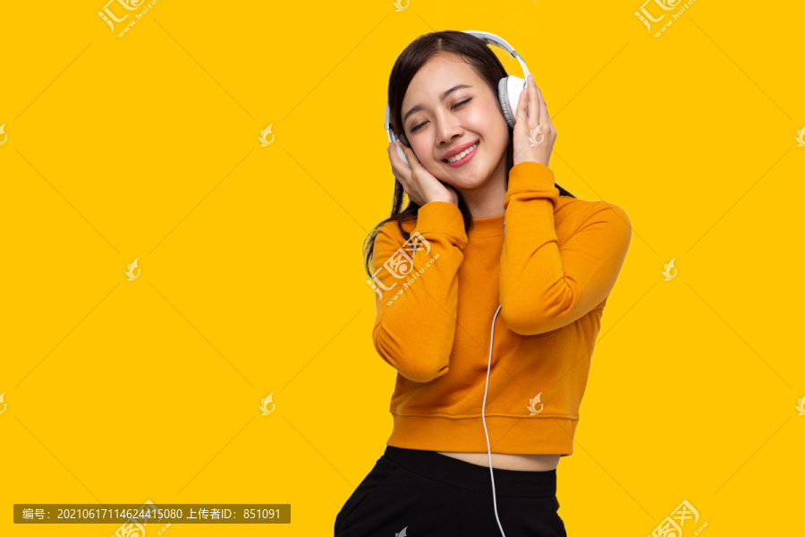 一幅快乐美丽的年轻亚洲女性的画像，戴着白色耳机听音乐，在黄色背景下独自跳舞和微笑