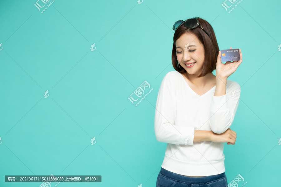 在绿色背景下，年轻、微笑、美丽的亚洲女子手持信用卡进行付款购物