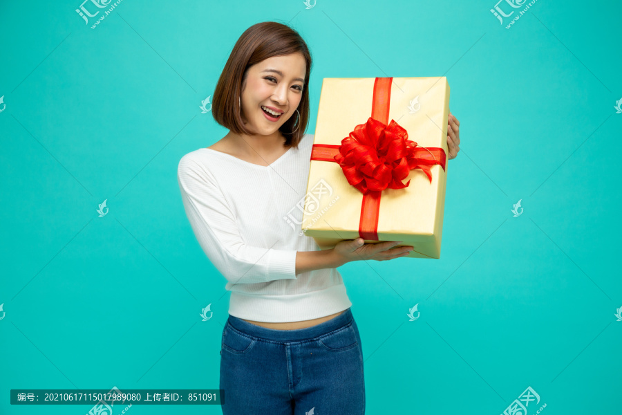 快乐美丽的亚洲女人微笑着，绿色背景上有一个金色的礼品盒。少女坠入爱河，接受情人的礼物。新年还是圣诞节