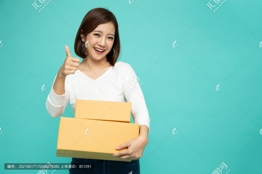 快乐的亚洲女人手持包裹盒，竖起大拇指，绿色背景，快递和运输服务理念