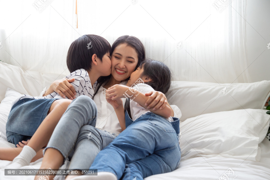 亚洲家庭的幸福与母亲、儿子和女儿在卧室的白色床上拥抱和亲吻母亲，感受幸福和家庭关系概念