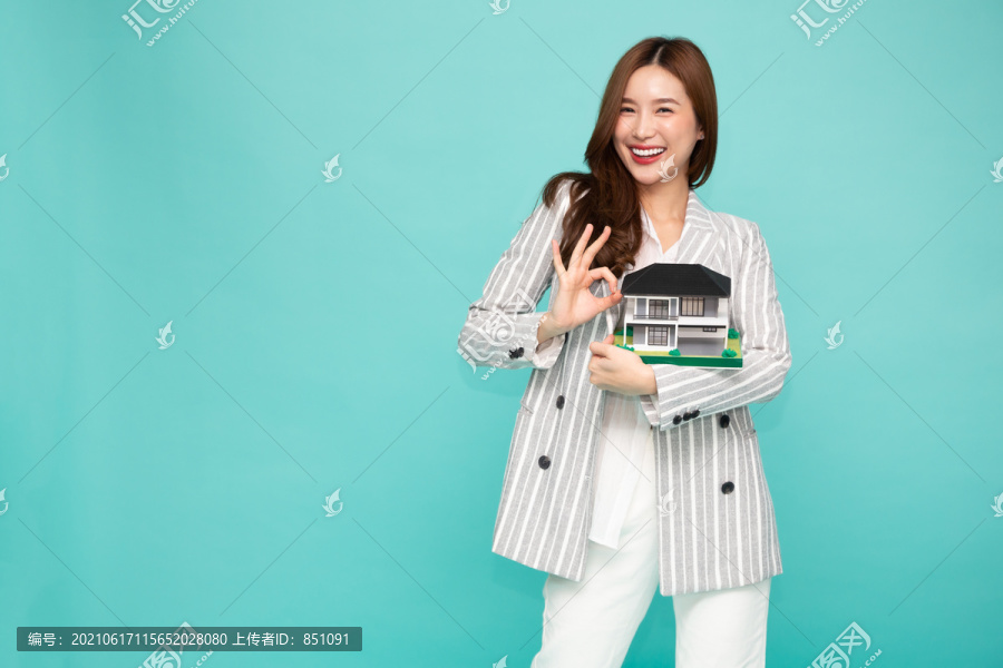 年轻的亚洲女性面带微笑，举着房子样本模型，与白色背景、房地产和家庭保险概念相隔离
