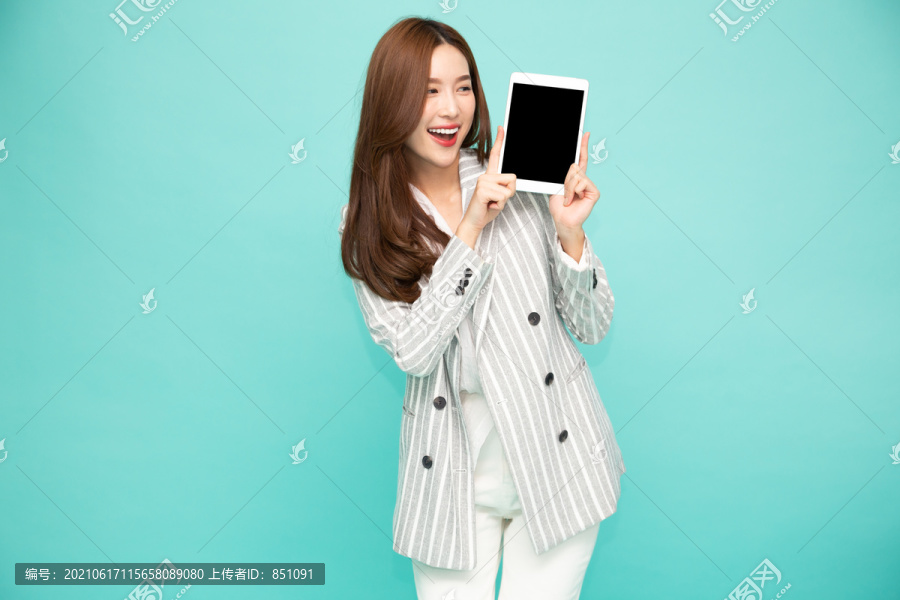 快乐的亚洲女人微笑着，手持平板电脑，背景为浅绿色