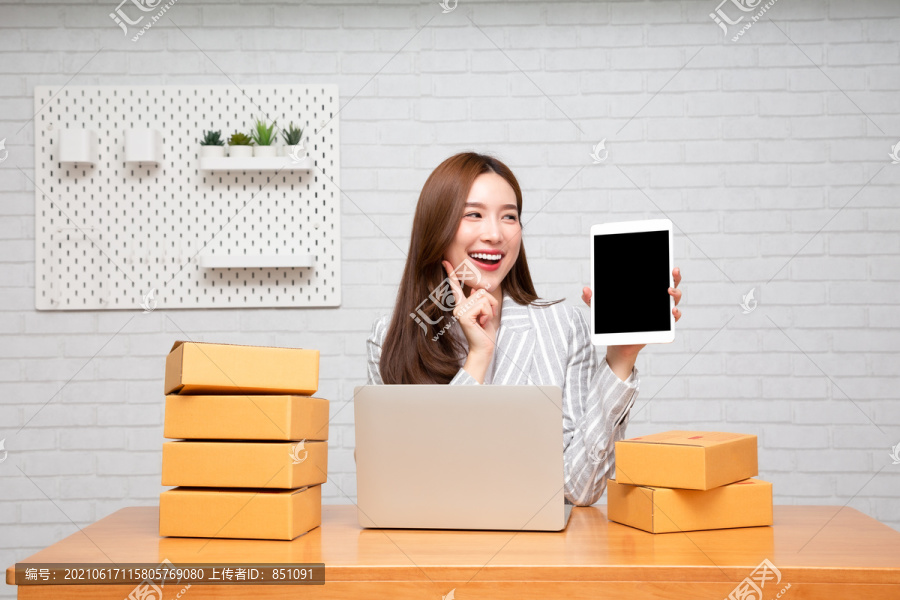 自由职业者年轻亚洲女性展示桌上带包裹盒的平板电脑