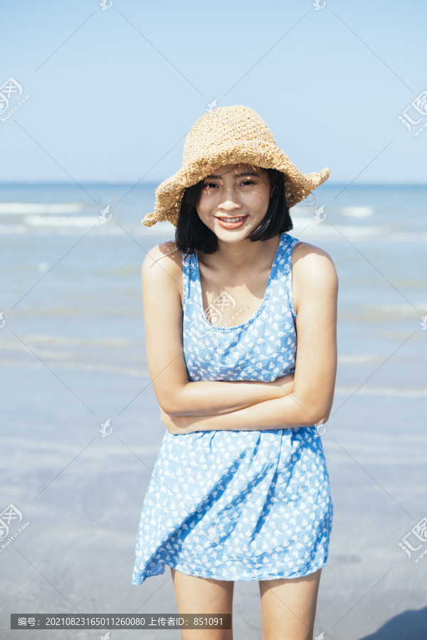 黑色头发，穿着蓝色连衣裙的可爱女孩微笑着欣赏风和海。