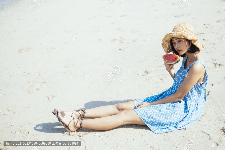 可爱的女孩伸着腿坐在海滩上，手里拿着西瓜。