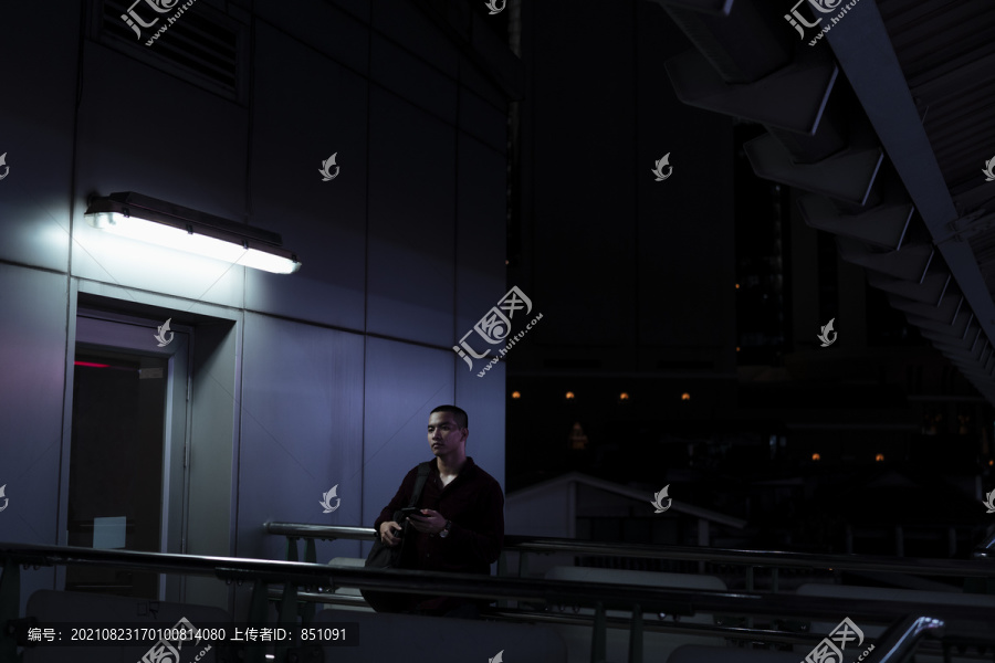 晚上，在空中火车站，一个穿着红衬衫的光头男人独自站在电梯或电梯前。