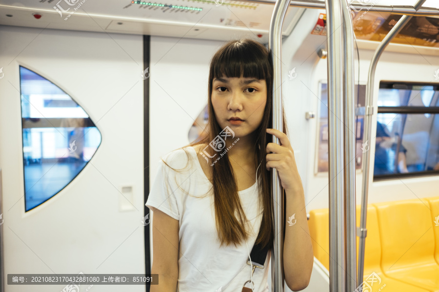 站在火车上，一位留着刘海发型的可爱泰国年轻女子抓着一根杆子，戴着耳机听音乐。