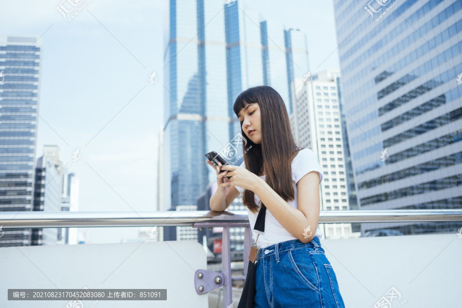 可爱的年轻泰国女孩刘海发型使用手机在城市。