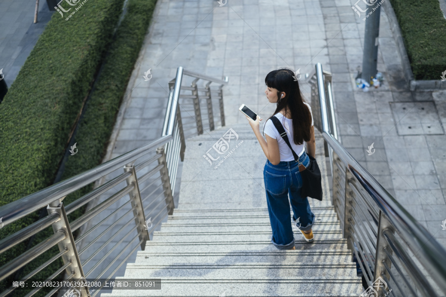 在城市里，一位年轻的时髦女人拿着智能手机走下楼梯。