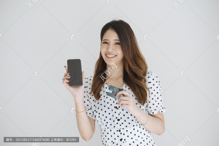 可爱的泰国年轻女子手持信用卡，随时准备购物，手机银行购物，数字购物，白色背景下的隔离。