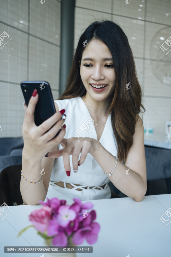 微笑的泰国女人喜欢在家里使用她的新智能手机。亚洲女孩使用手机，发短信，高兴地和男友发短信，看着智能手