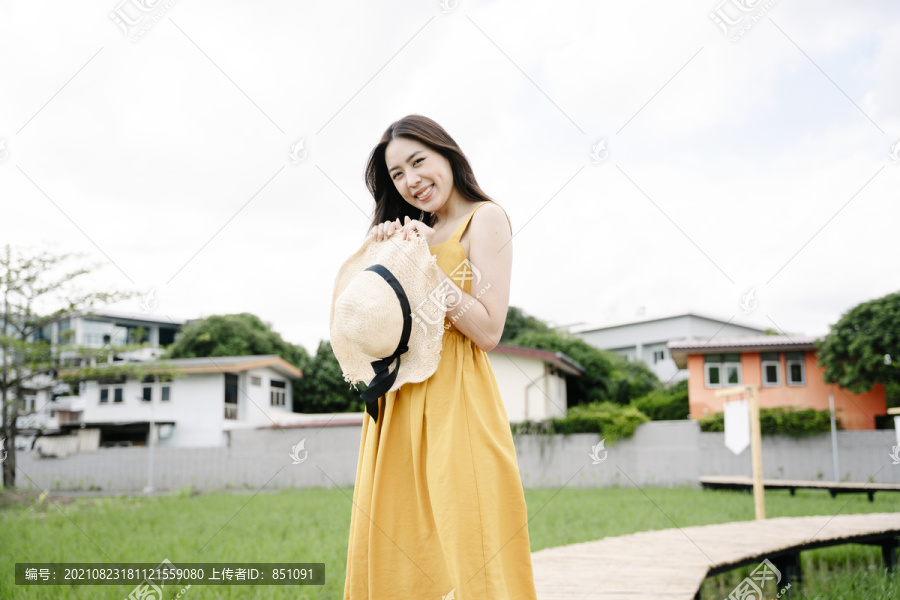 美丽的亚洲旅行家妇女手持帽子站在横跨稻田的木桥上的肖像。