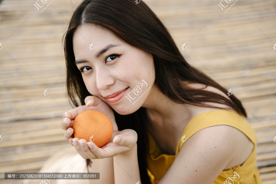 年轻亚洲女性的肖像，黑色头发，带橙色水果。健康生活理念。