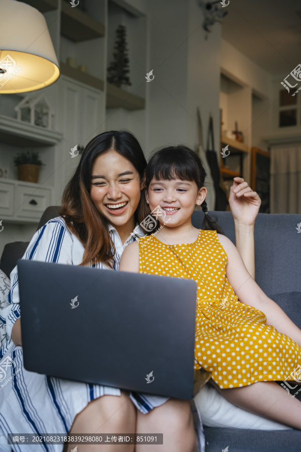 亚洲母亲和女儿在沙发上的笔记本电脑上看电影。