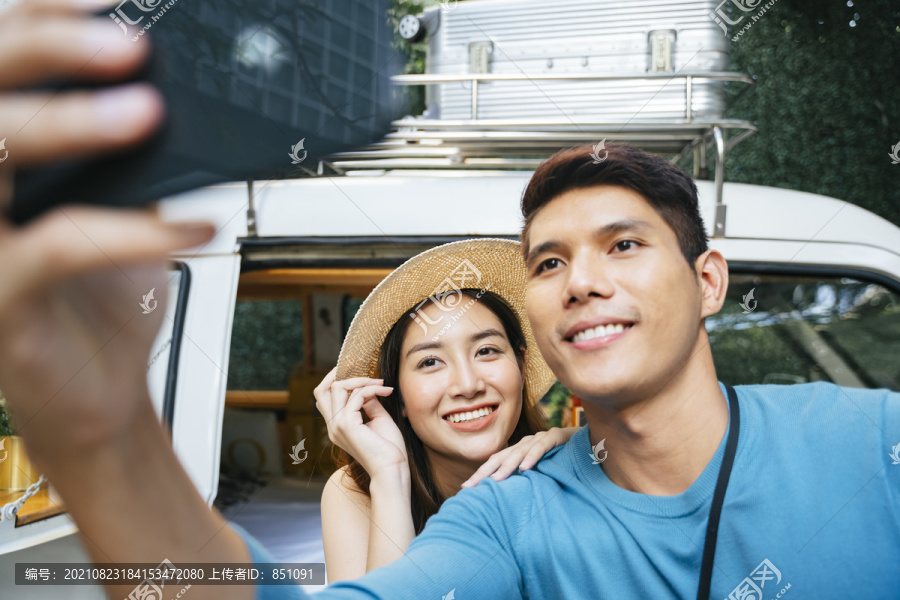 一对亚洲夫妇在露营地用智能手机站在车旁自拍。