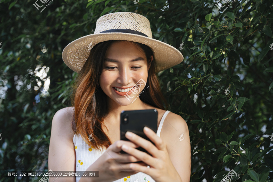 快乐快乐的亚洲女人戴着帽子在户外与智能手机聊天。