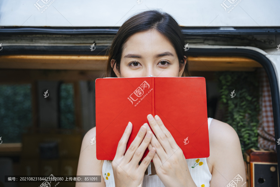 亚洲女人的特写肖像画用一本红皮书遮住她的嘴。