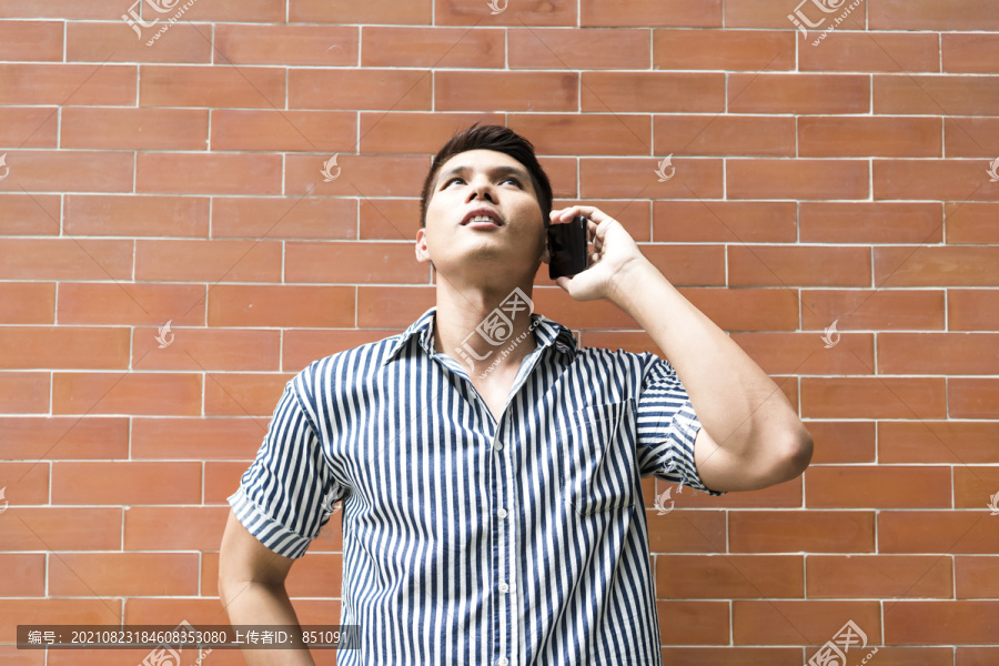 亚洲男人在砖墙背景下打电话。