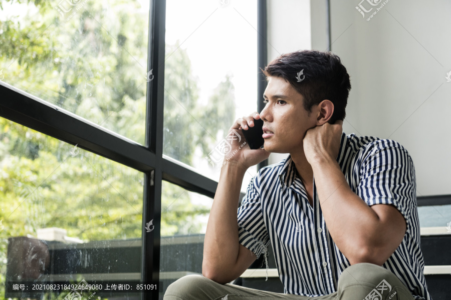 紧张的亚洲男人坐在家里的楼梯上，表情严肃地打电话。