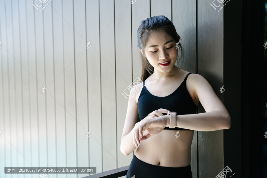 健康的亚洲女性穿着黑色运动内衣看着smartwatch。