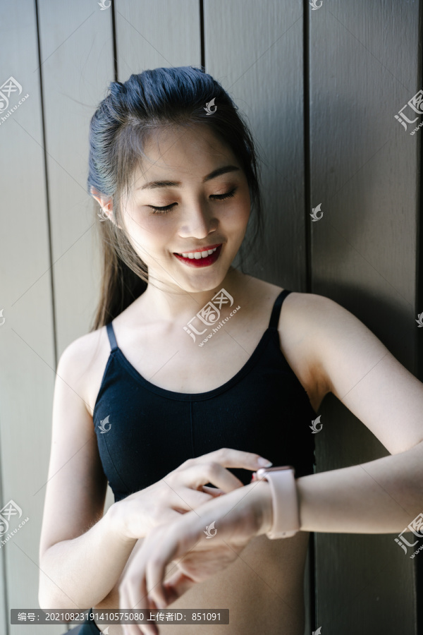 健康的亚洲女性穿着黑色运动内衣看着smartwatch。