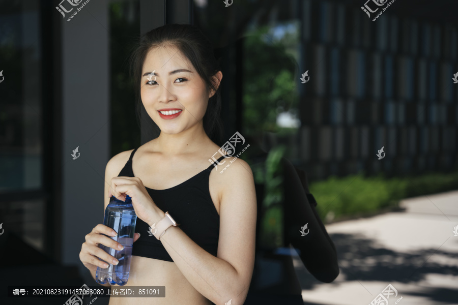 健康的亚洲女性在健身房喝瓶装水休息一下。